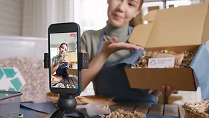 Asian young woman record video on TikTok IG reel Instagram shop happy side hustle showing off packaged product