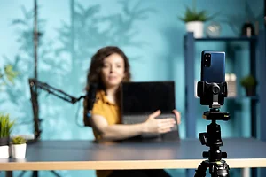 Focus on smartphone used by woman in studio to film laptop from brand sponsoring video, talking in microphone. Close up of phone used by content creator to do influencer marketing, promoting notebook