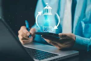 A businessman using a smartphone and laptop, with an overlay graphic showing an AI-powered financial transaction cycle between a bank/institution icon and a dollar/cash icon